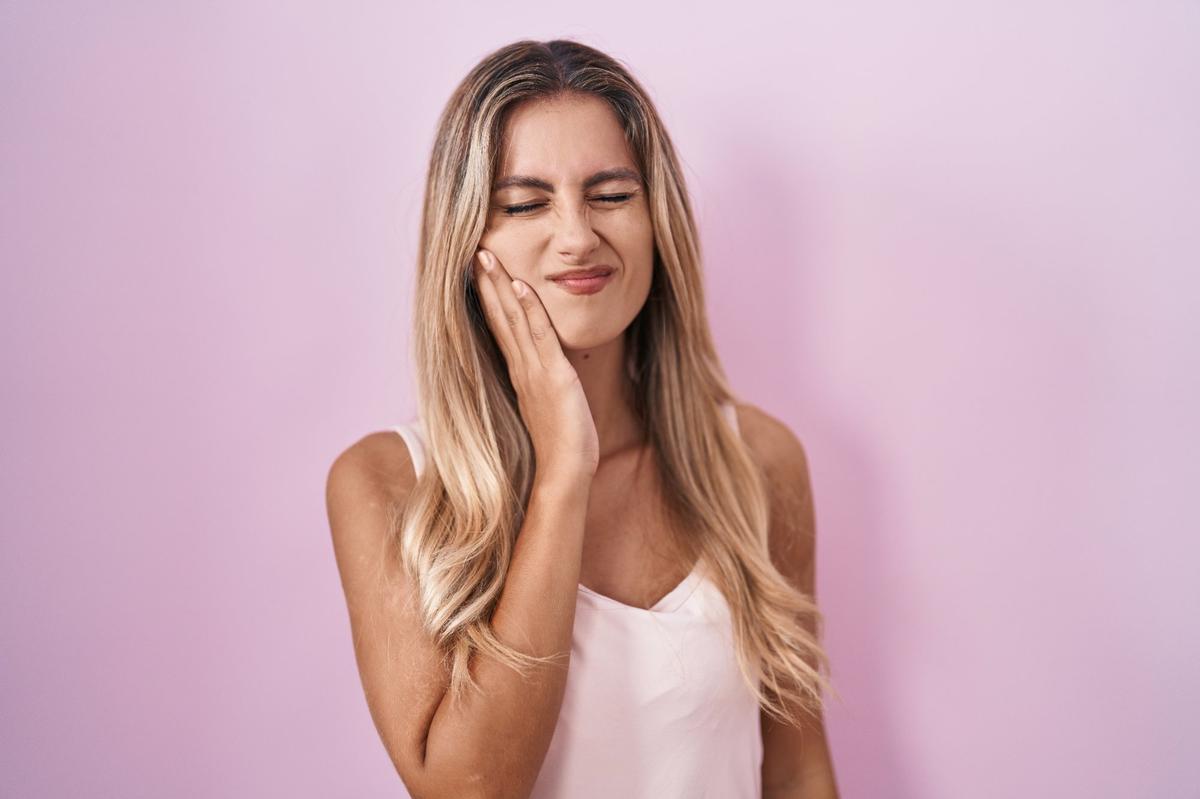 Mujer con sensibilidad dental tocándose la mejilla con dolor — consulta en Amadent Donostia